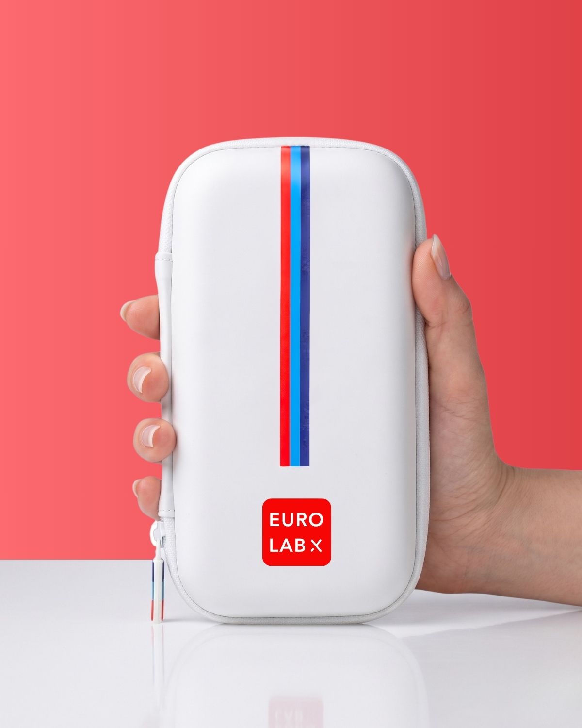 Hand holds a white portable medical case with a vertical red and blue stripe.
