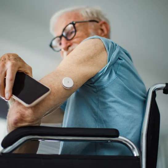 Senior man in wheelchair using smartphone to check his CGM