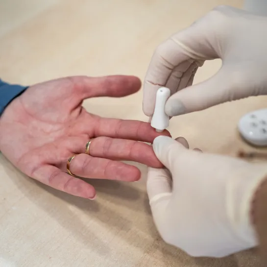 Hands of gloved pharmacist getting a blood sample from patient's hand