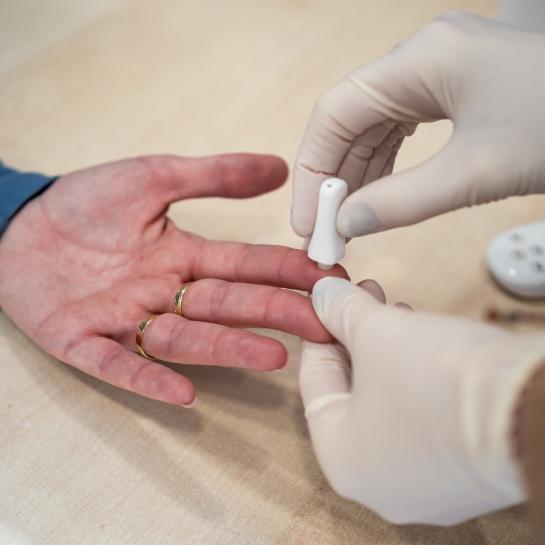 Hands of gloved pharmacist getting a blood sample from patient's hand