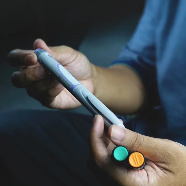 a person holding a grey diabetes injector pen in one hand and two vials in the other hand.