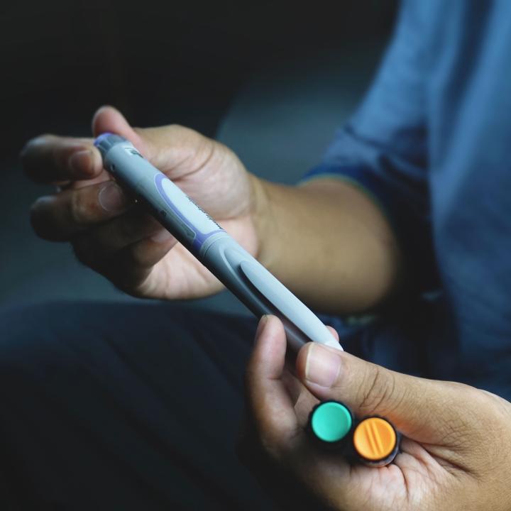 a person holding a grey diabetes injector pen in one hand and two vials in the other hand.