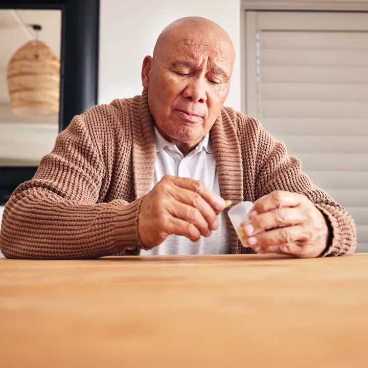 Senior Man At Home Sitting At Table Taking Medication From Bottle