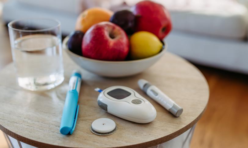 Close up on a table with a bowl of fruit, a glass of water, and diabetes testing supplies