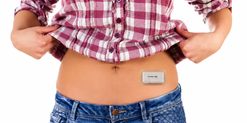 Person lifting shirt to show insulin delivery patch on the abdomen.