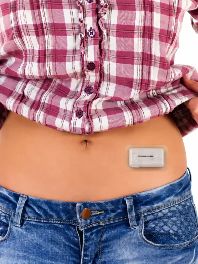 Person lifting shirt to show insulin delivery patch on the abdomen.